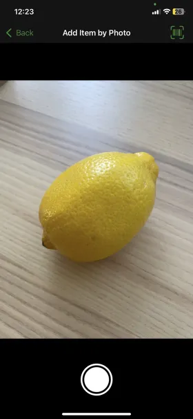 OurGroceries' Add Item by Photo screen, with the camera pointed at a lemon on a wooden table and a shutter button below